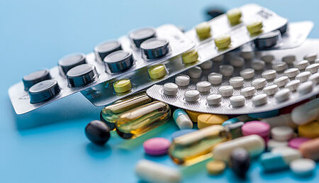 Various blister packs of pills and loose capsules arranged on a blue background, representing pharmaceutical products, medication variety and healthcare treatment options.