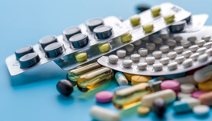 Various blister packs of pills and loose capsules arranged on a blue background, representing pharmaceutical products, medication variety and healthcare treatment options.