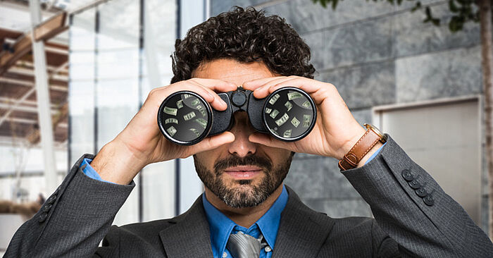 Businessman looking through binoculars with money reflected in the lenses, symbolizing financial foresight or opportunity scanning.