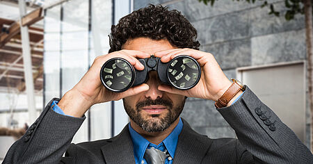 Businessman looking through binoculars with money reflected in the lenses, symbolizing financial foresight or opportunity scanning.