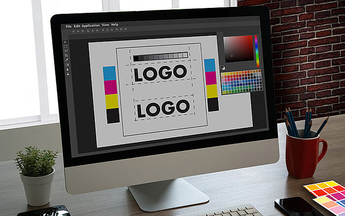Graphic designer using a computer to create a company logo, with color palette visible.
