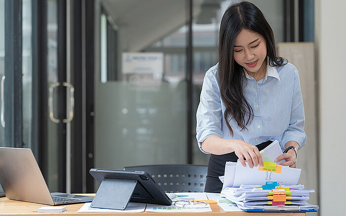 Businesswoman working with stacks of paper files, searching and checking documents of multiple regions.
