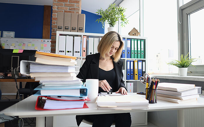Office worker stamps paperwork at a desk, with documents and a laptop nearby.