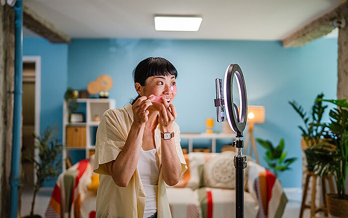 Japanese woman live streaming while reviewing makeup and cosmetic products at a table.
