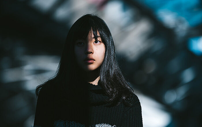 A young Asian woman standing outdoors looks worried, her face half-shaded.