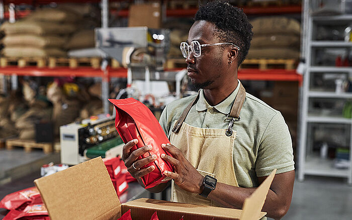 A man examines bags of coffee beans in a warehouse prior to distribution.