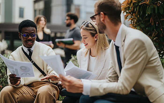 A diverse team of professionals outdoors reviewing documents together.