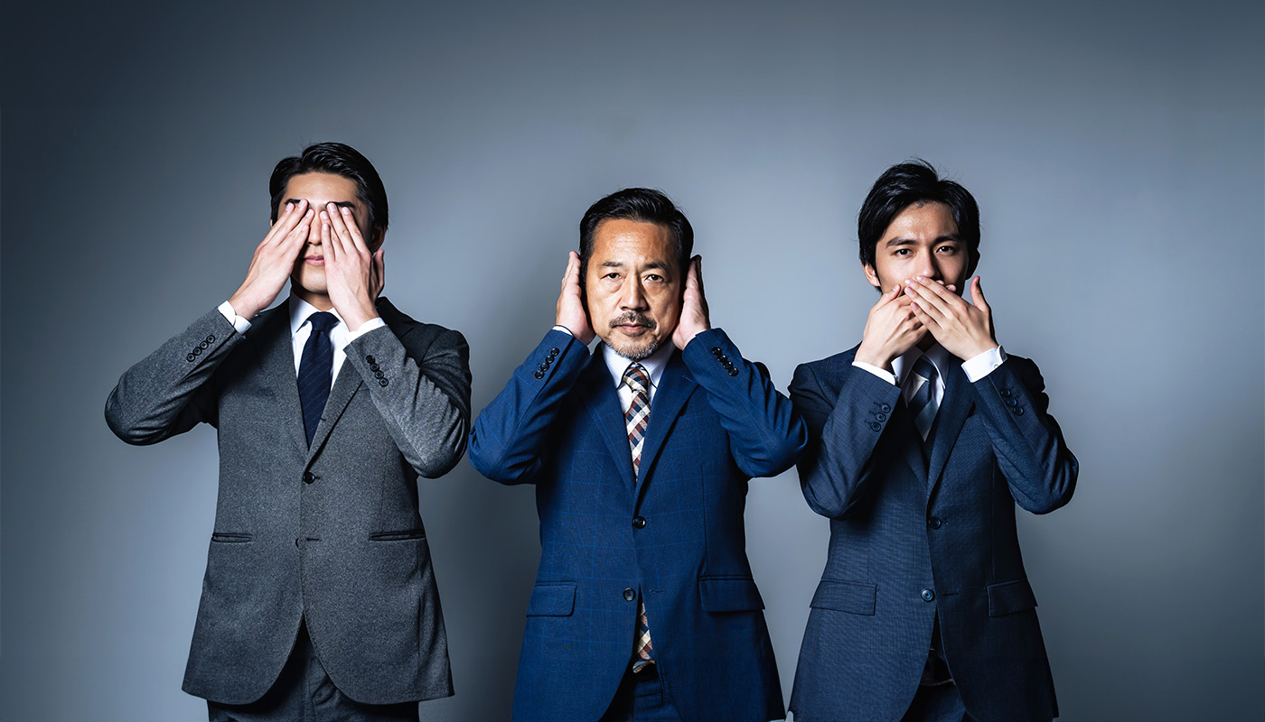 Three businessmen in suits, each covering either their eyes, ears or mouth with their hands, symbolizing the concept of “see no evil, hear no evil, speak no evil” in a corporate setting.